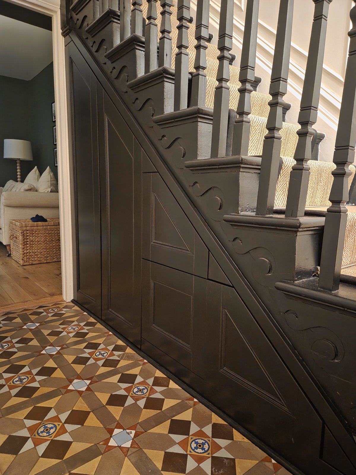 Painted staircase with panelled understairs above a patterned tiled hallway