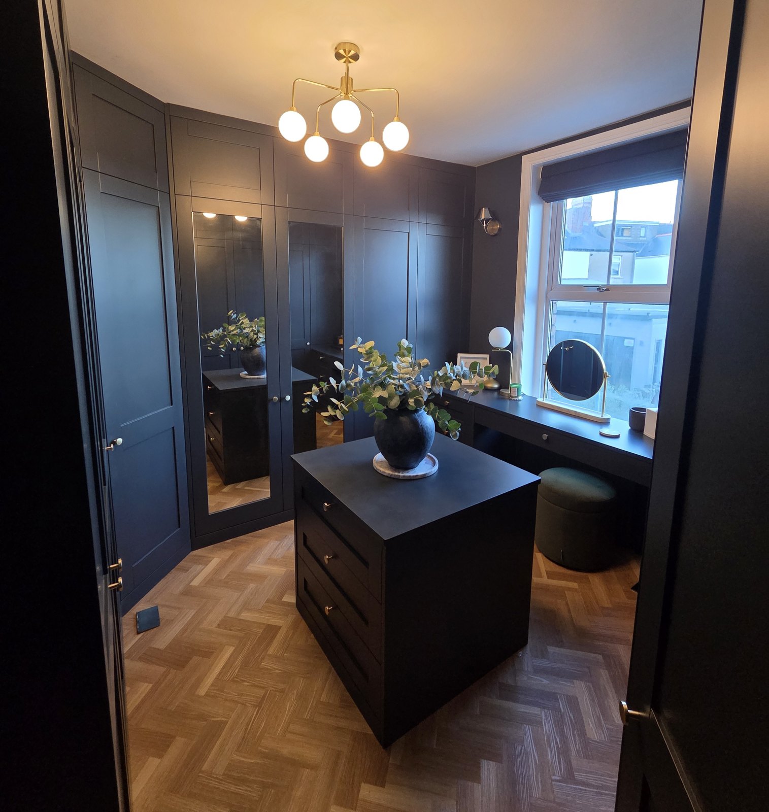 Dark navy dressing room with a central island of drawers and herringbone flooring
