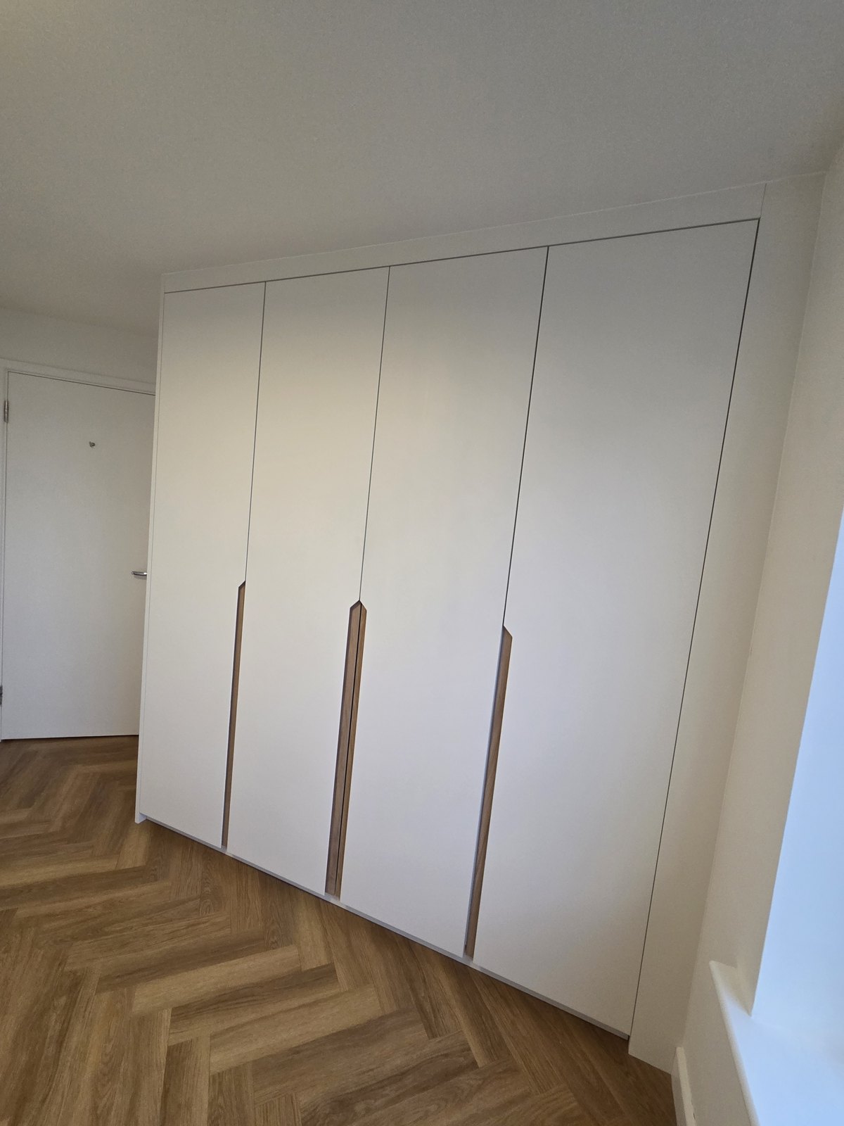 Handleless fitted wardrobes with slim vertical pulls on herringbone flooring