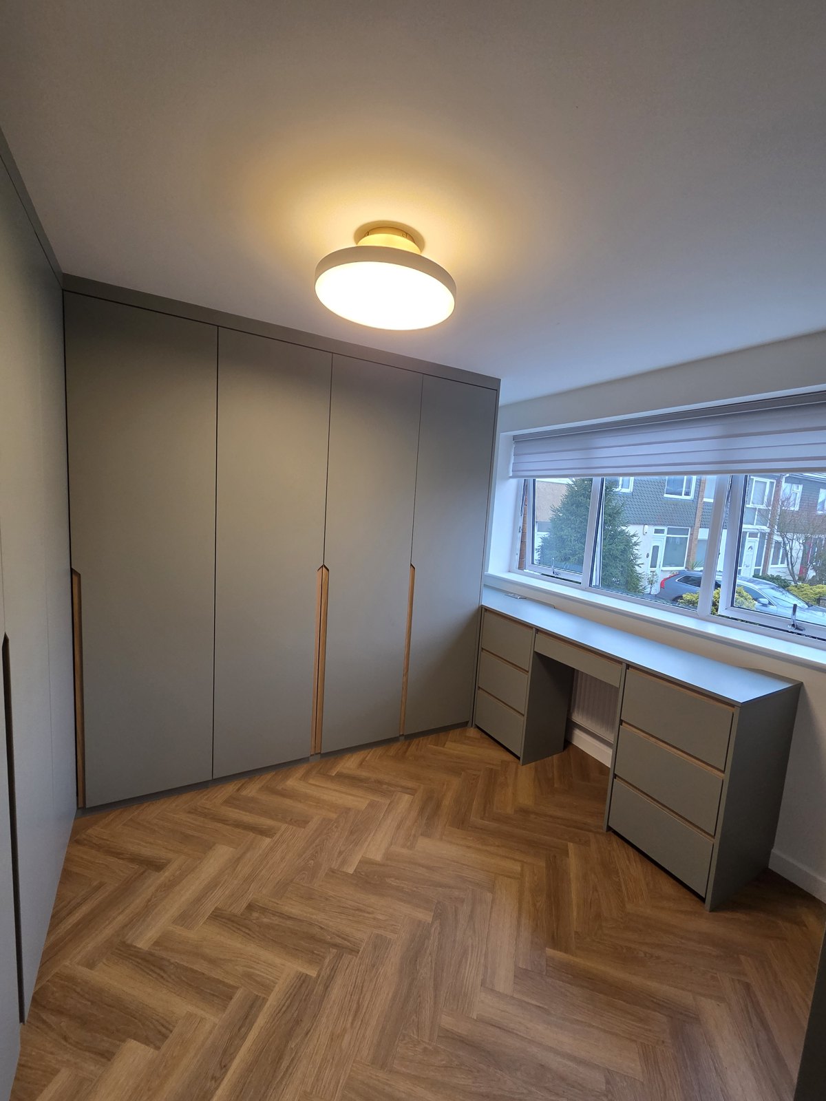 Grey fitted wardrobes with a built-in desk and drawer unit under a window