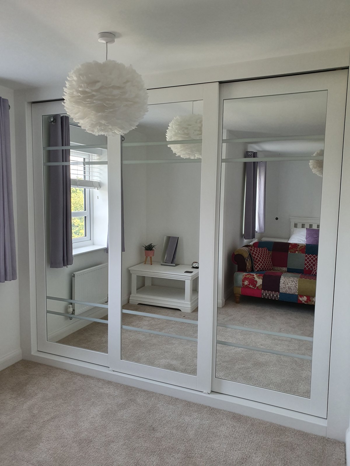 Full-height mirrored sliding wardrobe doors reflecting a bedroom
