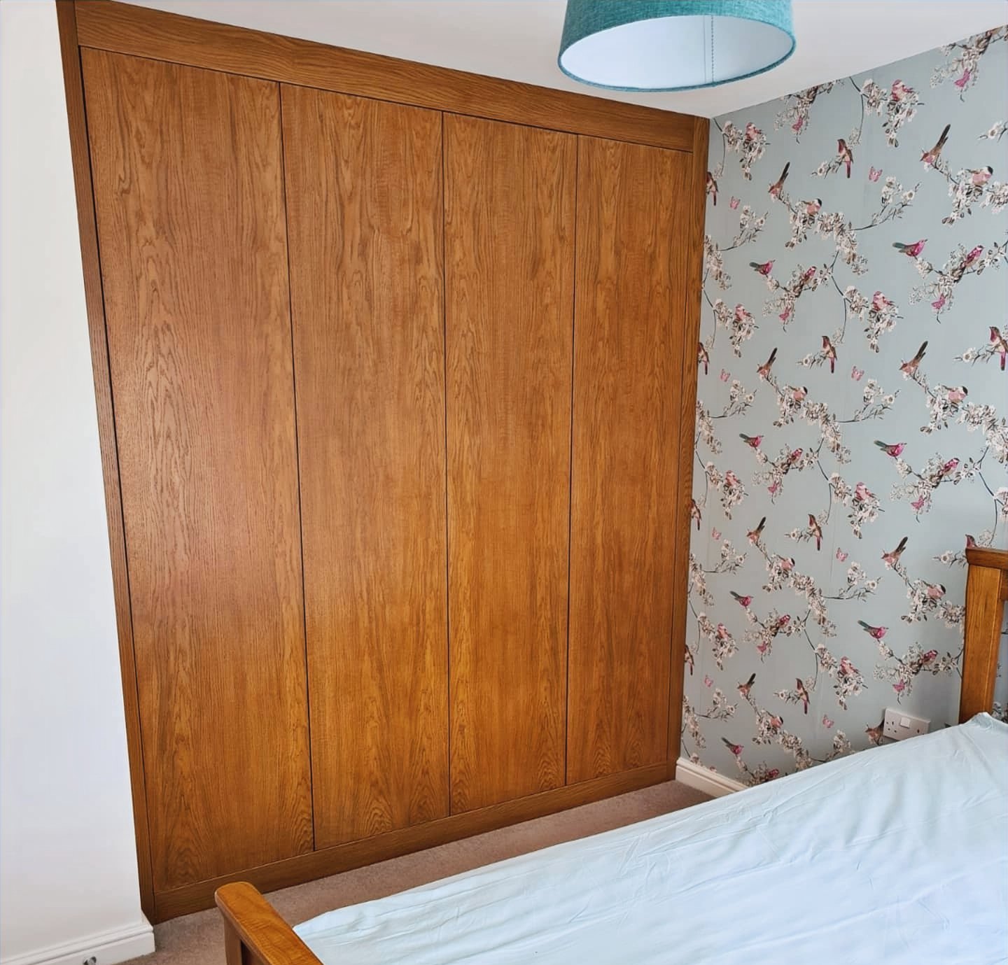Oak panelled feature wall behind a bed next to patterned wallpaper