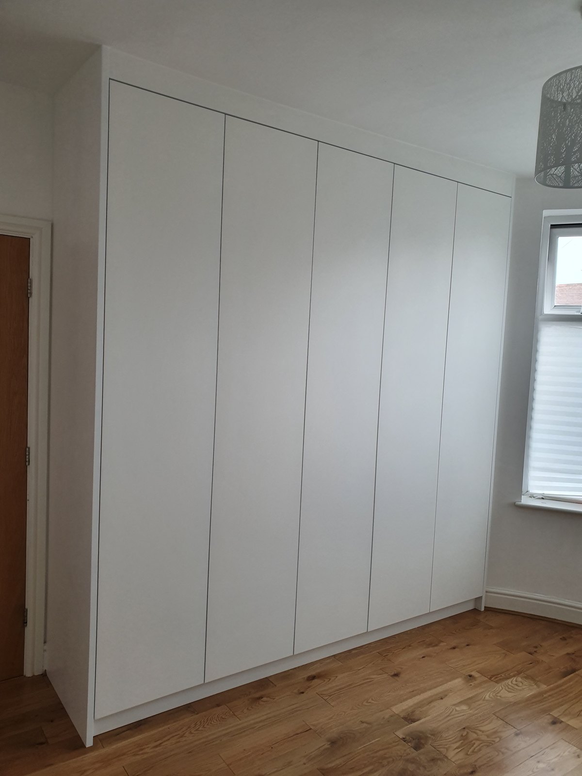 Tall white fitted wardrobes running into the corner of a bedroom