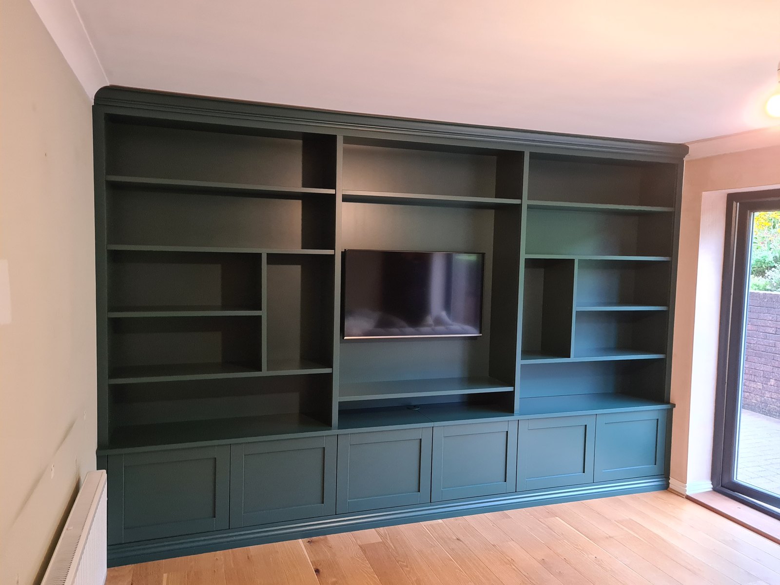 Built-in dark green living room shelving with TV recess and cupboards below