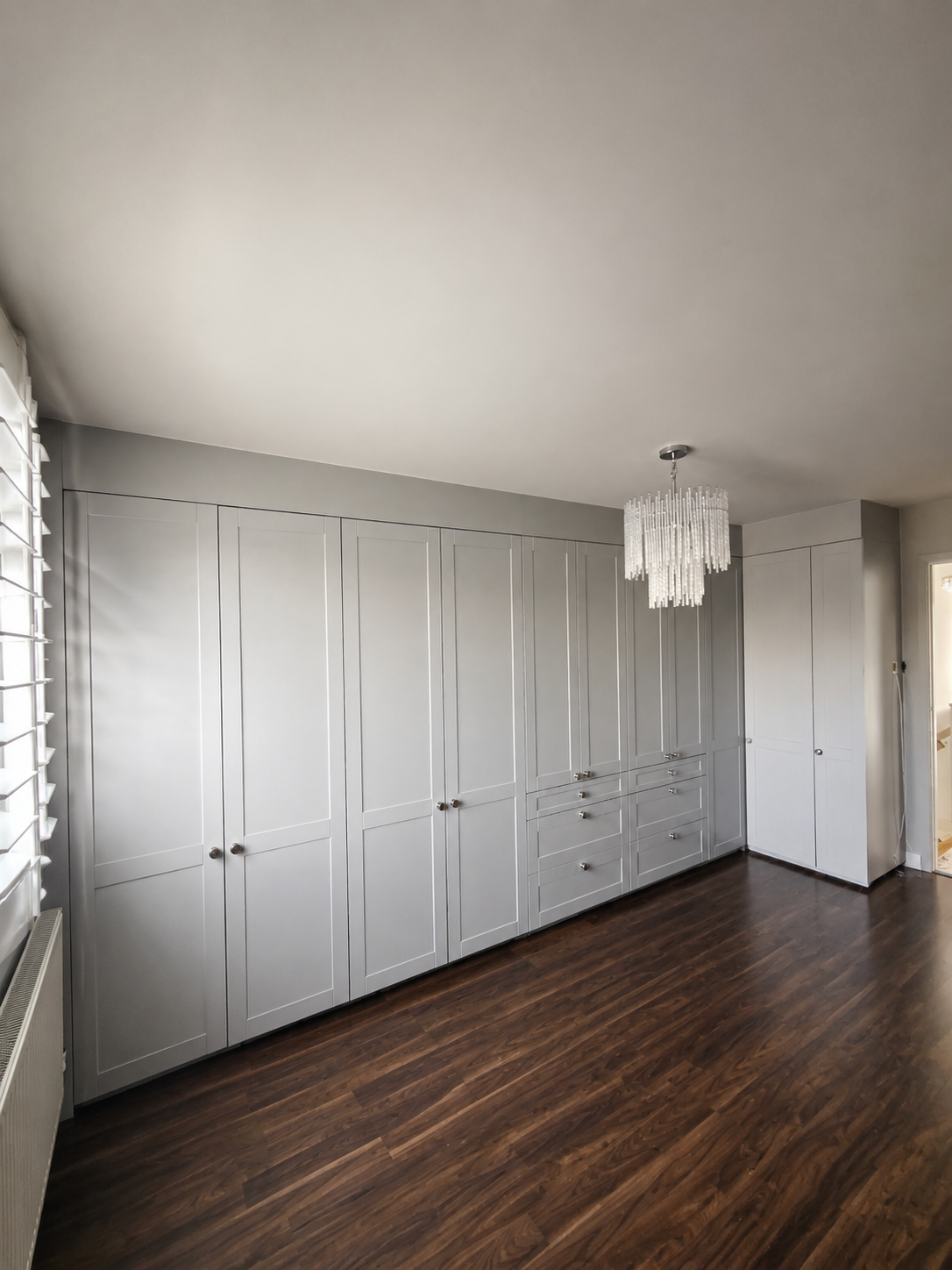Wren grey Shaker-style fitted wardrobes wall-to-wall with round silver knobs on a dark wood floor