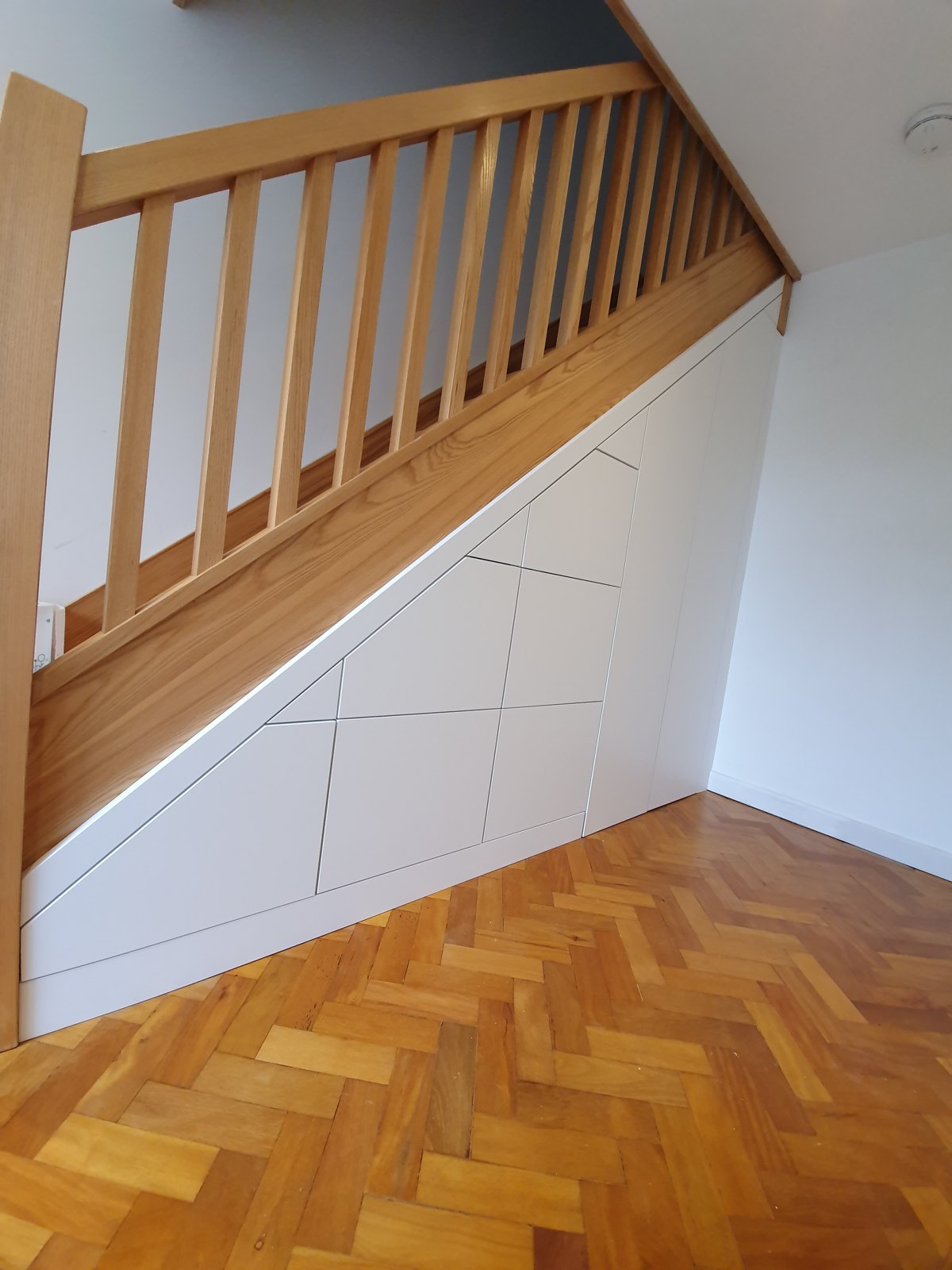 Under-stairs storage fitted beneath an oak staircase on parquet flooring